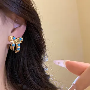Close-up of vintage gold bow-knot earrings with blue zircon flowers on ear