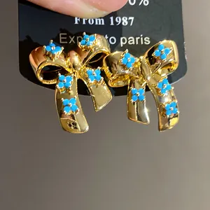 Detail view of gold bow earrings with blue floral clover patterns.