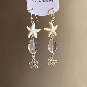 Detail view of starfish and oval glass bead drop earrings with flower charm accents