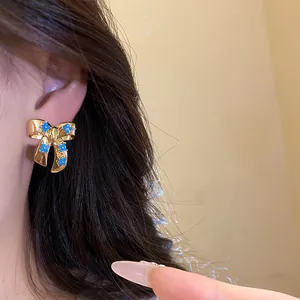 Detail of a vintage gold bow earring with blue zircon flowers worn on model's ear