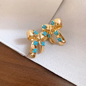Macro view of vintage gold bow stud earrings featuring delicate small turquoise flowers