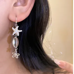 Detail shot of elegant beach-style starfish and flower drop earrings worn on ear.