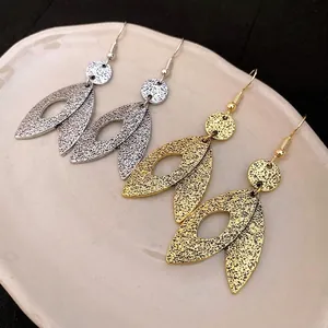 Elegant minimalist hammered gold and silver leaf drop earrings displayed on a ceramic tray