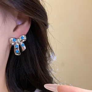 Detailed view of a silver-toned bow stud earring featuring blue zircon flower accents on ear