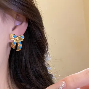 Detailed close-up of gold-plated bow stud earring with blue floral stones worn on the ear.