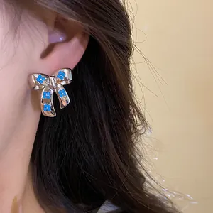 Detailed view of silver bow-tie stud earrings with blue floral zircon accents