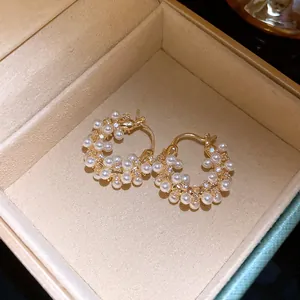 Macro shot of gold-plated hoop earrings with pearls and zircons inside a beige box