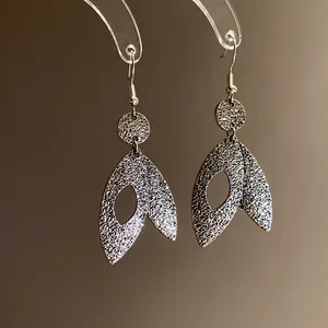 Macro detail of elegant silver leaf pendant earrings featuring a shimmering textured surface