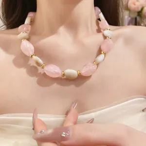 Detailaufnahme einer unregelmäßigen Acrylperlenkette in Rosa und Creme am Hals des Modells
