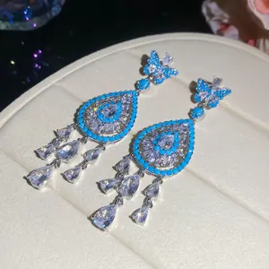 Macro detail of teardrop zircon earrings featuring turquoise inlay and butterfly motifs