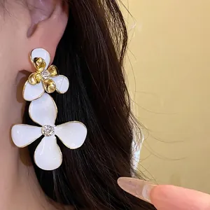 Elegant vintage white enamel flower drop earrings with sparkling rhinestones on model.