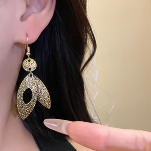 Close-up of gold leaf dangle ear hook earrings with textured metal finish on wearer.