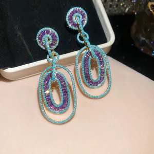 Close-up of luxury drop earrings featuring purple zircons and turquoise bead accents