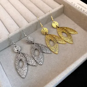 Close-up of leaf-shaped dangle earrings in gold and silver finishes with hammered texture