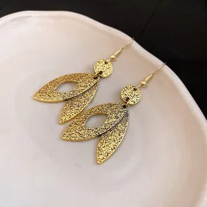 Detailed macro close-up of vintage textured gold leaf-shaped dangle earrings on plate