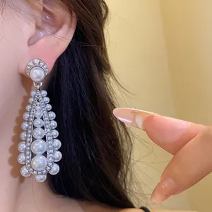 Macro close-up of vintage teardrop pearl dangle earrings with silver needle on model ear