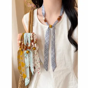 Detailed view of floral and plaid chiffon necklaces with wooden beads on a linen shirt