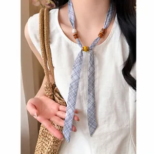 Detail of summer plaid chiffon scarf necklace with wooden beads on white linen top