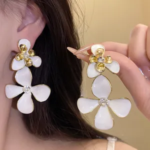 Detail view of elegant white enamel flower drop earrings with rhinestones for women.