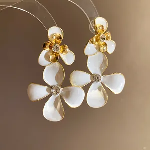 Close-up of white enamel flower pendant earrings with sparkling rhinestones and gold edges.