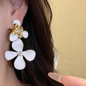 Close-up detail of elegant white enamel flower drop earrings with sparkling rhinestone centers