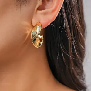 Vue détaillée d'une boucle d'oreille créole géométrique torsadée en or portée par un modèle