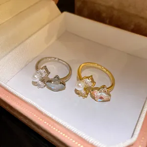 Primo piano di anelli aperti a fiore in oro e argento con perle e zirconi in scatola regalo.