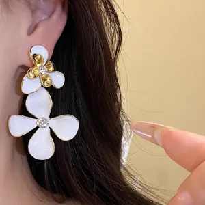 Close-up detail of white enamel flower drop earrings with sparkling rhinestones