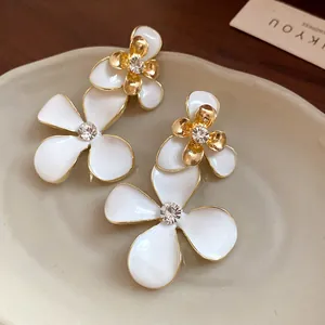 Macro view of vintage white enamel flower earrings with gold edges and central crystals.