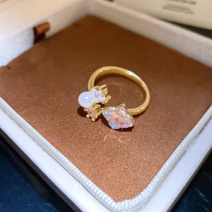 Dettaglio di un elegante anello a fiore dorato con perla e pietra cangiante di lusso