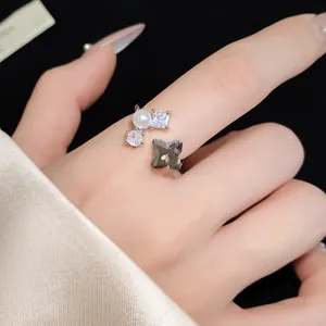 Dettaglio di un anello aperto con perle, zirconi quadrati e un ciondolo a fiore.