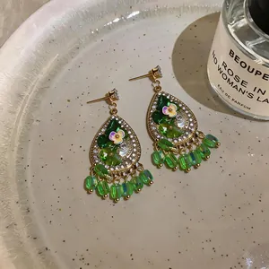 Close-up of green teardrop earrings with floral design, crystals and bead dangles.