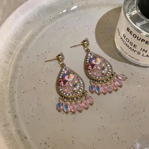 Close-up of ornate water-drop earrings featuring sparkling crystals and pink beads on a plate