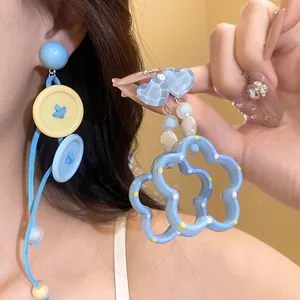 Vue détaillée des boucles d'oreilles dopamine bonbon cœur bouton pompon bleu et jaune.