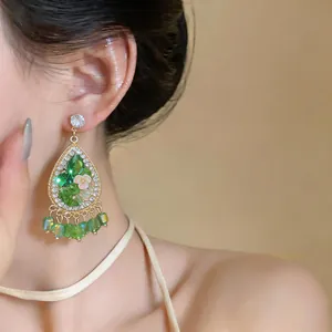 Detailed view of green teardrop earrings with floral accents and sparkling crystals.