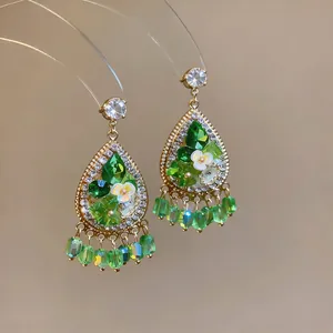Close-up of French palace style water drop earrings with green crystals and floral details.