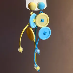 Détail de boucles d'oreilles pompons boutons bleu et jaune avec cordons colorés