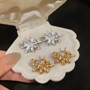 Close-up of zircon flower stud earrings in gold and silver within a shell-shaped box.