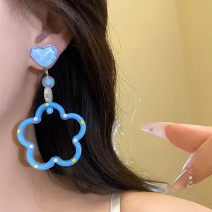 Vue détaillée d'une boucle d'oreille pendante cœur et fleur bleu vif portée sur l'oreille