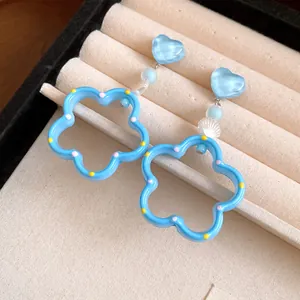 Vue détaillée en gros plan de boucles d'oreilles cœur et fleur bleu pastel dans une boîte à bijoux