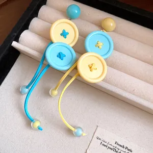 Vue détaillée des boucles d'oreilles à pompon bouton colorées en bleu et jaune.