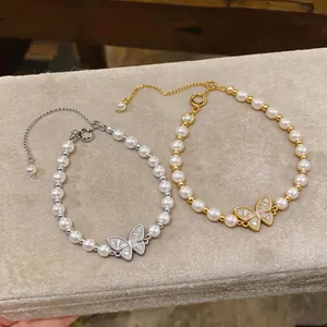 Dettaglio di braccialetti di perle con ciondolo a farfalla in oro e argento.