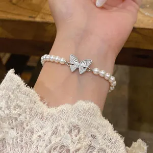 Primo piano di un elegante bracciale di perle con ciondolo a farfalla d'argento al polso