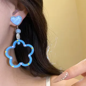 Détail montrant un clou d'oreille cœur bleu avec créole en forme de fleur sur un mannequin.