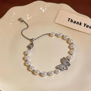Dettaglio di un bracciale di perle a farfalla placcato oro 18 carati su un piatto crema