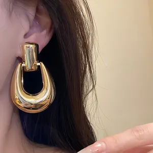 Primo piano di una donna che indossa un grande orecchino a forma di U dorato.