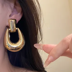 Primo piano di orecchini dorati lucidi a forma di U in metallo indossati da modella