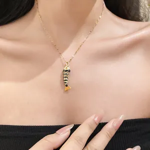 Close-up of an elegant black and gold enamel fish pendant necklace worn by a model.
