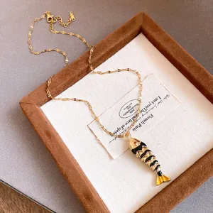 Close-up detail of the gold-plated fish pendant necklace featuring black enamel dripping oil