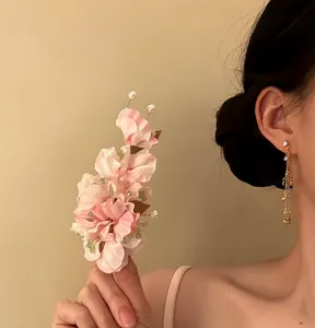 Hand holding a delicate pink fabric flower hair clip with pearl accents and beads